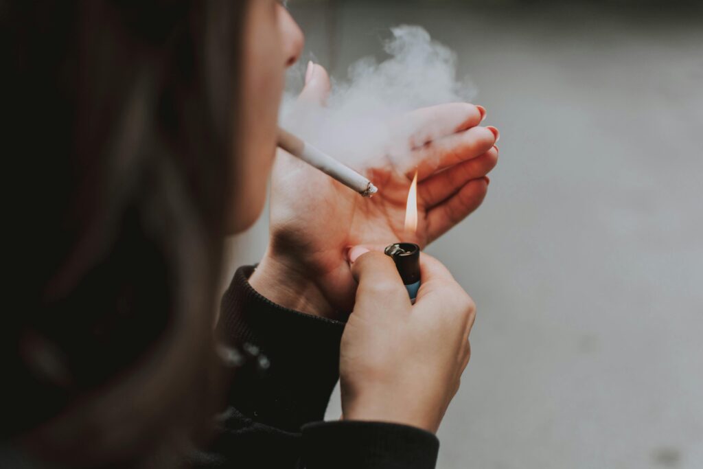 pexels-photo-2827798-2827798 Close-up of a woman lighting a cigarette outdoors with a lighter, smoke visible.